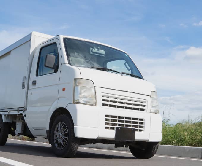 青空の下、道路を走行中の白い軽貨物トラック。